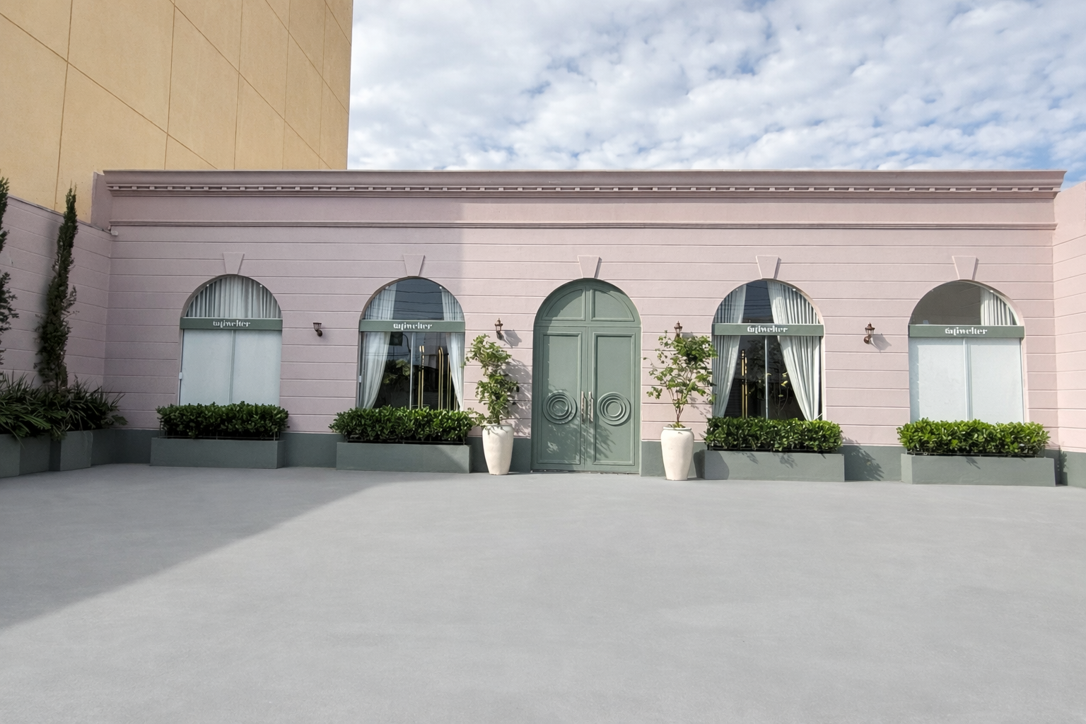Fachada rosa do Tati Welter Authentic Spa com porta verde em arco e jardineiras, na Av. Isaac Póvoas em Cuiabá